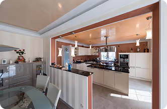 Moderne offene Küche mit weißen Schränken, schwarzen Arbeitsflächen und Essbereich mit Glastisch und Stühlen.