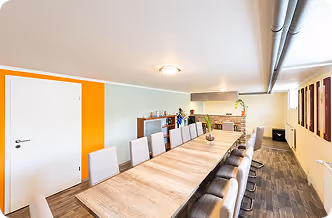 Moderner Konferenzraum mit langem Holztisch und grauen Stühlen an beiden Seiten.