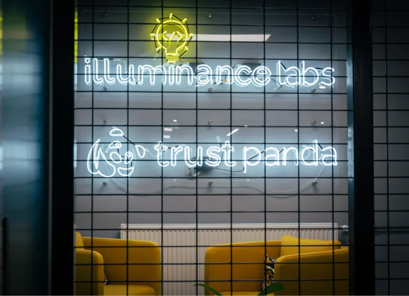 Office room with neon signs saying illuminance labs and trust panda, with yellow chairs in front.