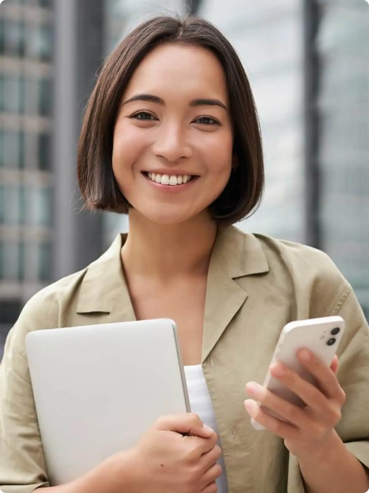 Smiling businesswoman holding a laptop and using a smartphone outdoors