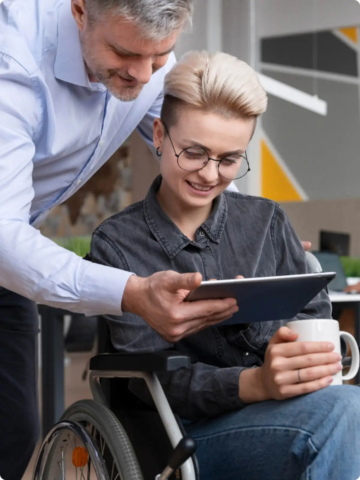 Man assisting a woman in a wheelchair with a tablet in a modern office