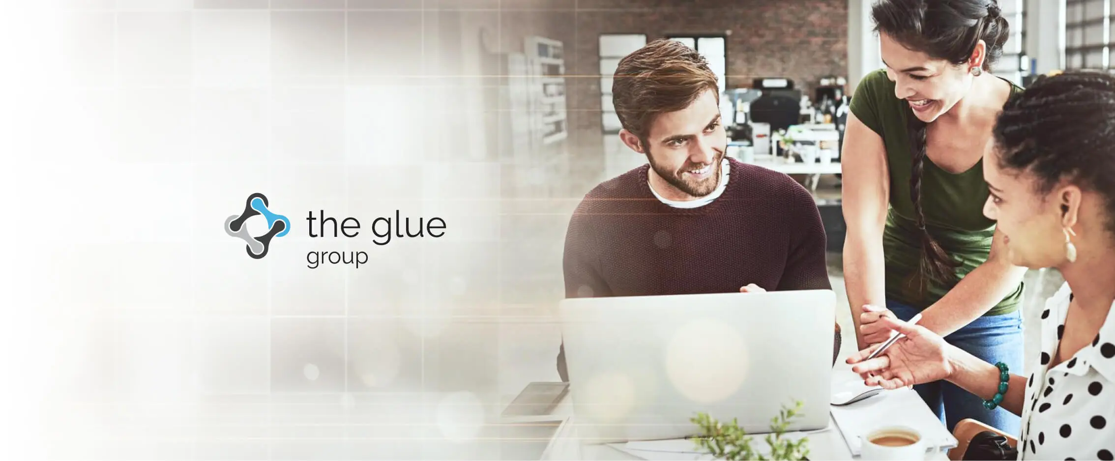 The Glue Group logo beside a smiling man working on a laptop while two colleagues look on