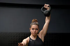 Žena drží kettlebell nataženou paží nad hlavou
