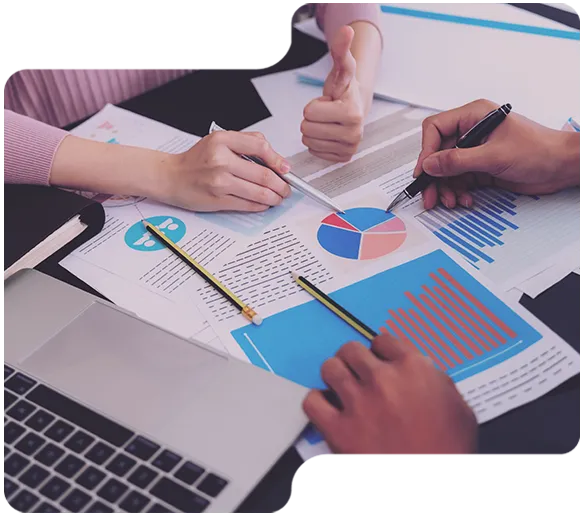 Zwei Personen analysieren Diagramme und Diagramme bei einem Meeting mit Laptop und Stiften auf einem Tisch.