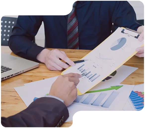 Zwei Geschäftspersonen analysieren Diagramme auf einem Klemmbrett und Papier am Schreibtisch.