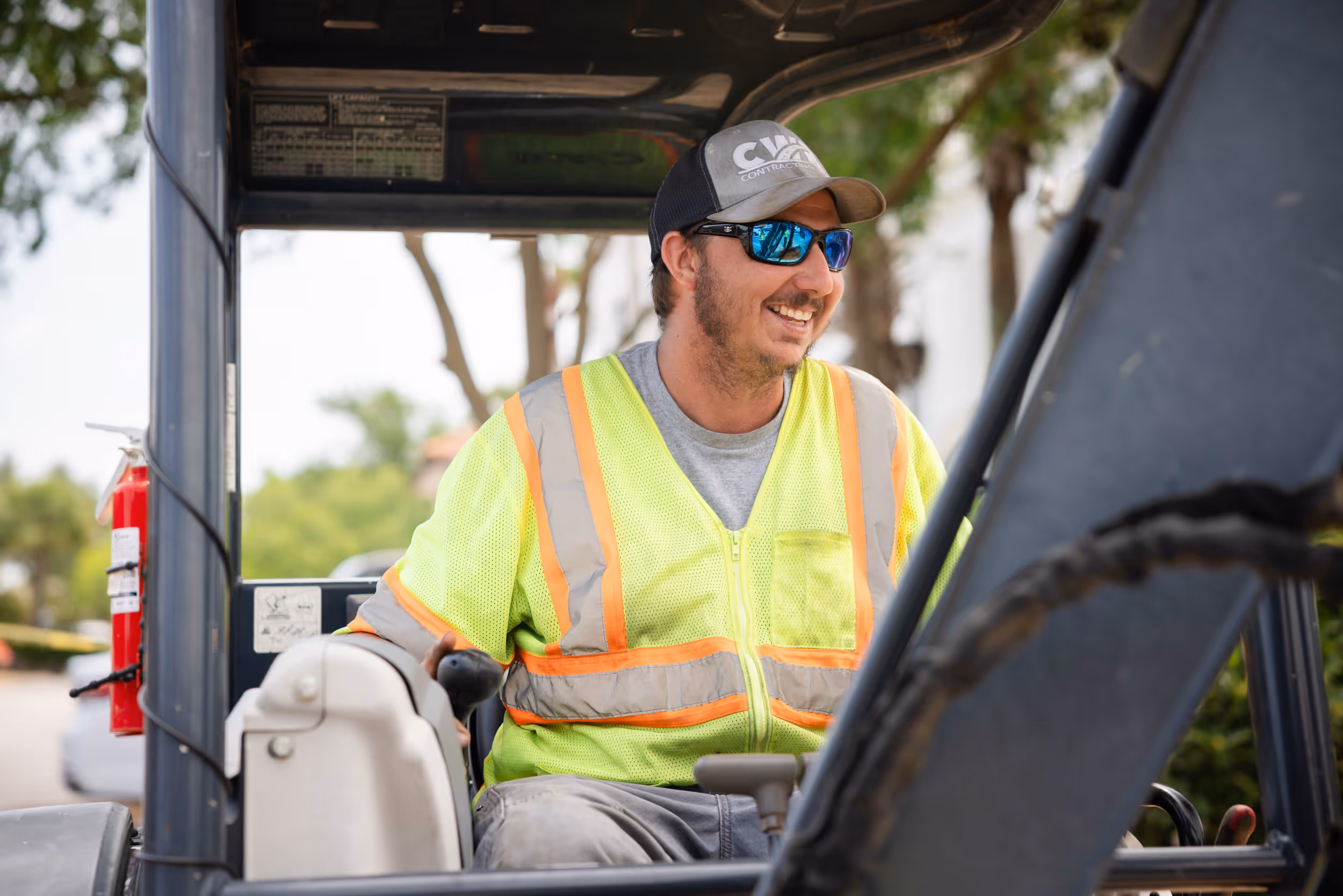 Smiling construction worker in a high-visibility safety vest and cap operating heavy machinery outdoors.