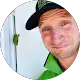 Smiling man with a beard wearing a black cap and lime green shirt in a circular frame.
