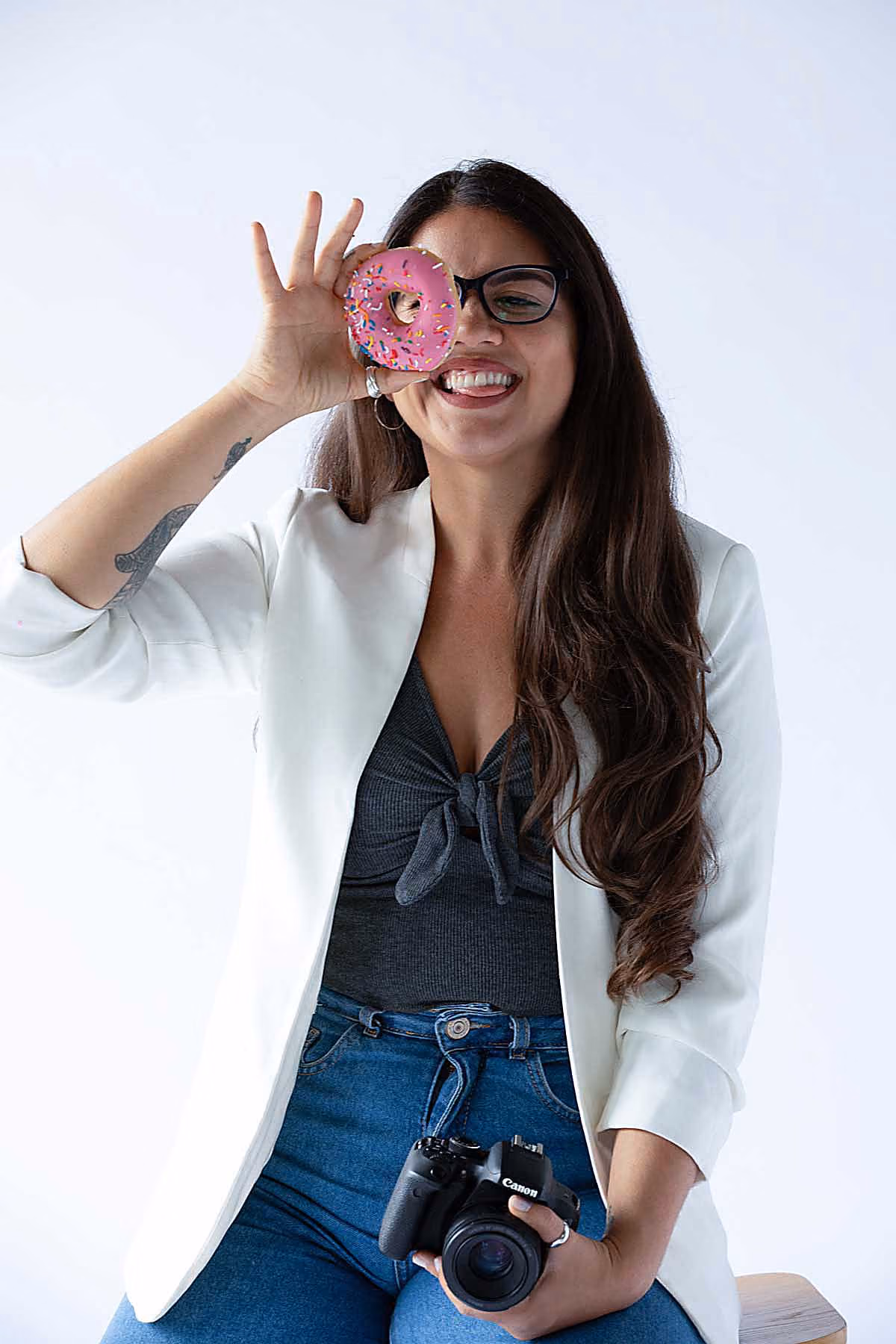 RealClicks team member Bianca Borges holding a pink sprinkled donut in front of one eye and a Canon camera