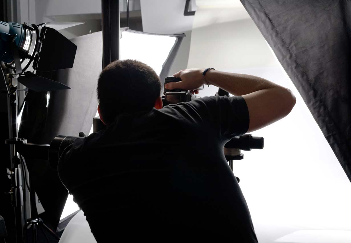 Photographer from behind taking a picture with a camera in a studio setup with bright softbox lights and equipment around.