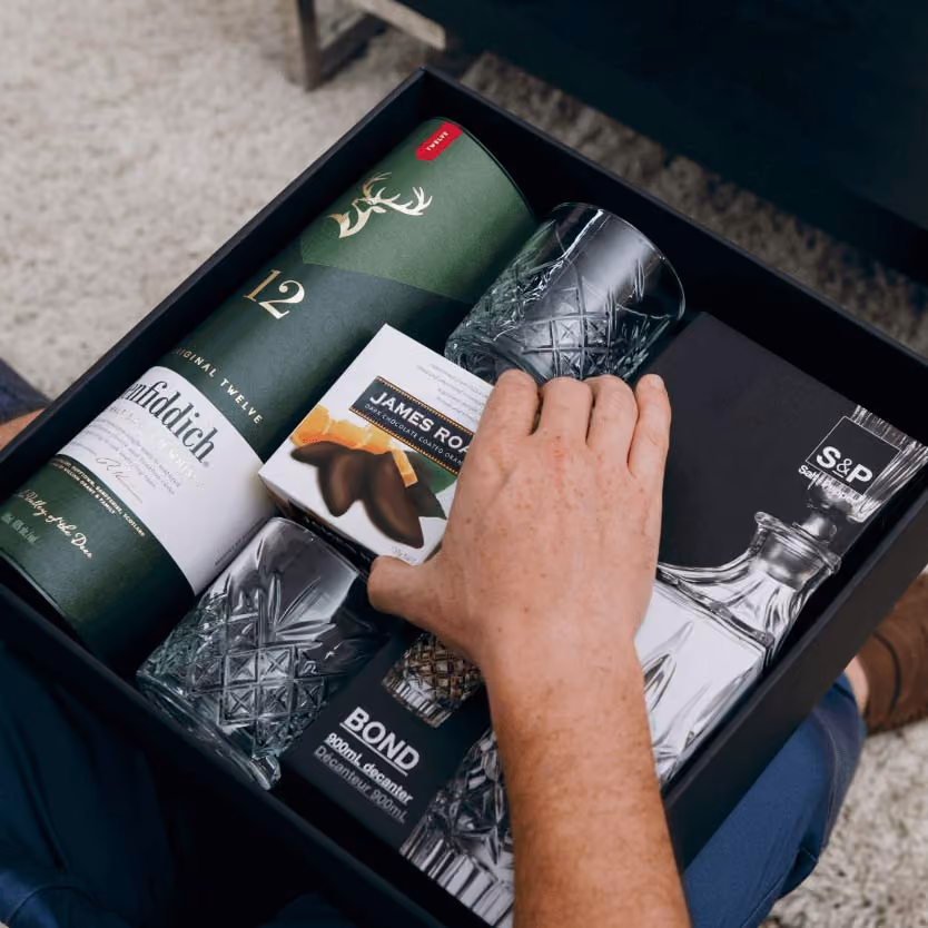 A man's hand reaching into a Gourmet Basket hamper grabbing a chocolate product