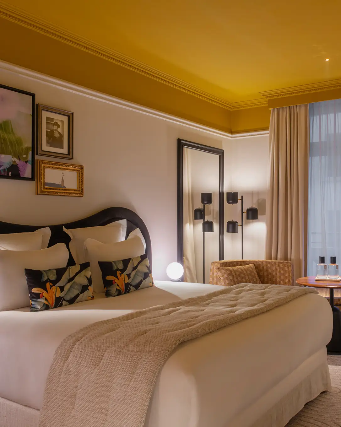 Quarto elegante com cama branca, almofadas estampadas, luminária, poltrona de vime e espelho