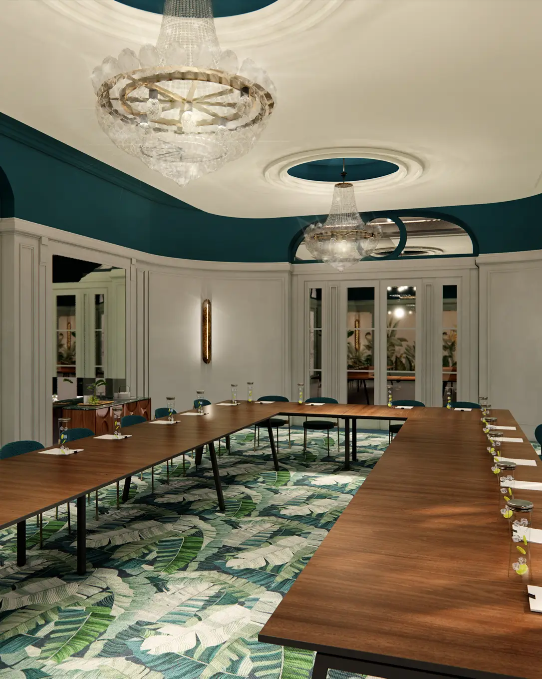 Sala de reuniões elegante com mesas em forma de U, tapetes com estampa de folhas verdes e grandes lustres de cristal.
