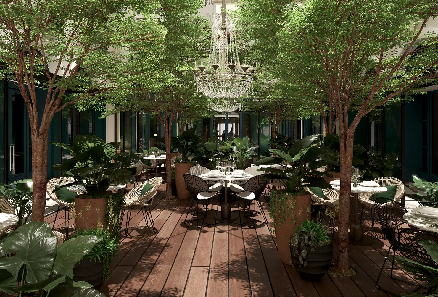 Sala de jantar interna com plantas grandes, mesas redondas e dois grandes lustres de cristal.