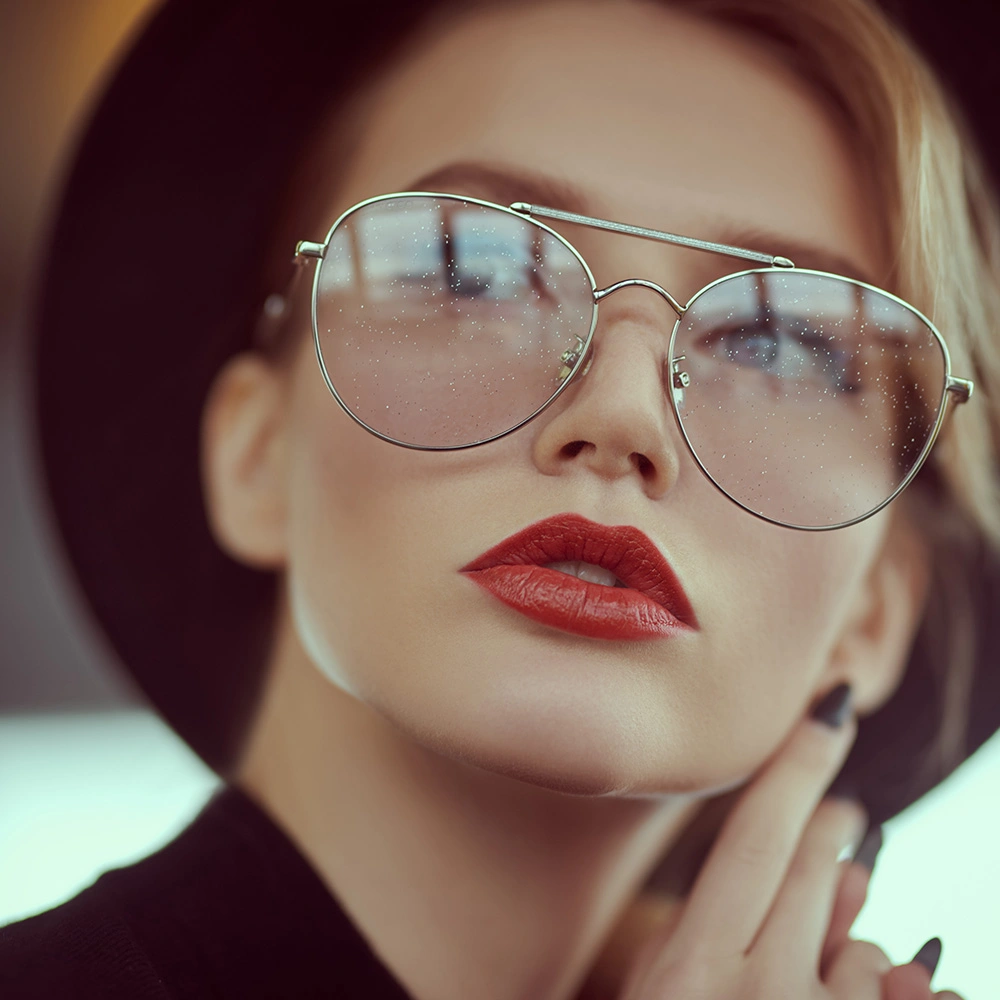 Nahaufnahme einer Frau mit roten Lippen, die eine schwarze Sonnenbrille und einen schwarzen Hut trägt.
