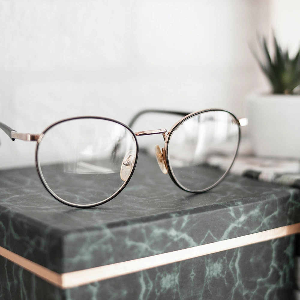 Eine Brille mit dünnem Metallgestell liegt auf einer grünen Marmorbox mit goldfarbenem Rand.