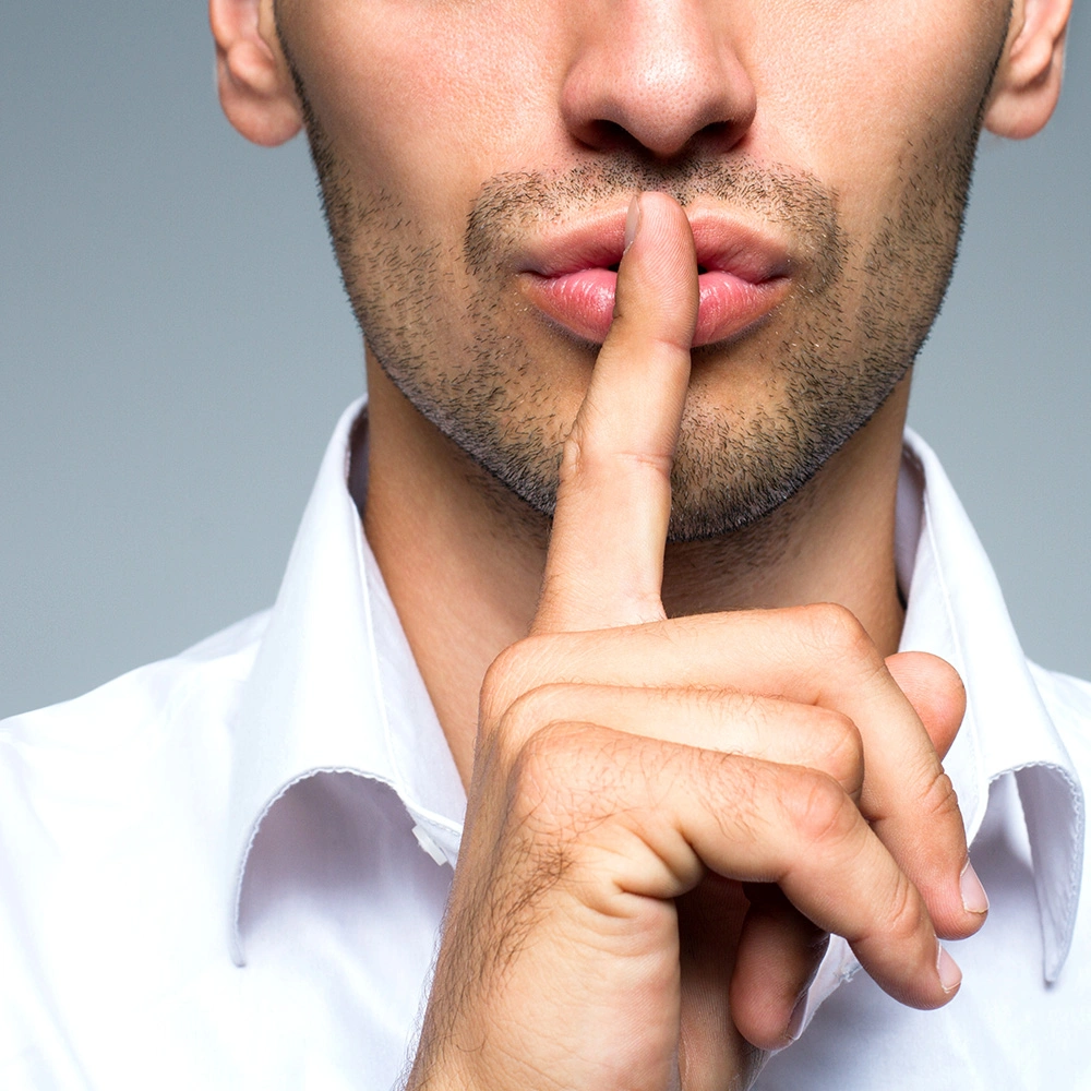 Ein Mann legt seinen Zeigefinger auf die Lippen als Zeichen für Ruhe.