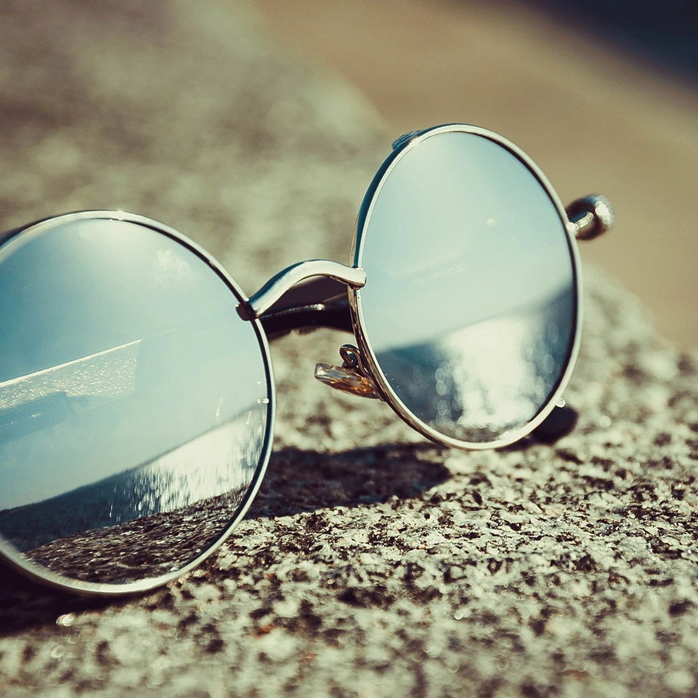 Runde verspiegelte Sonnenbrille liegt auf einer rauen Steinoberfläche und reflektiert das Sonnenlicht.