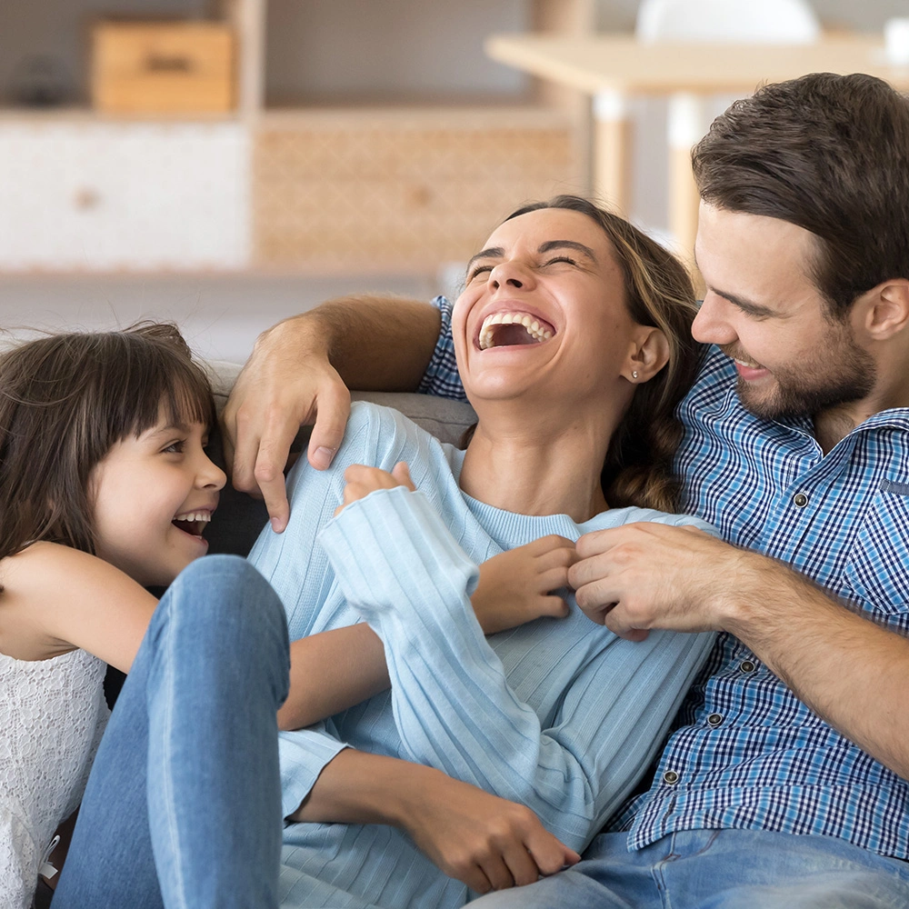 Glückliche Familie mit lachender Mutter, Vater und Tochter, die gemeinsam auf dem Sofa sitzen.
