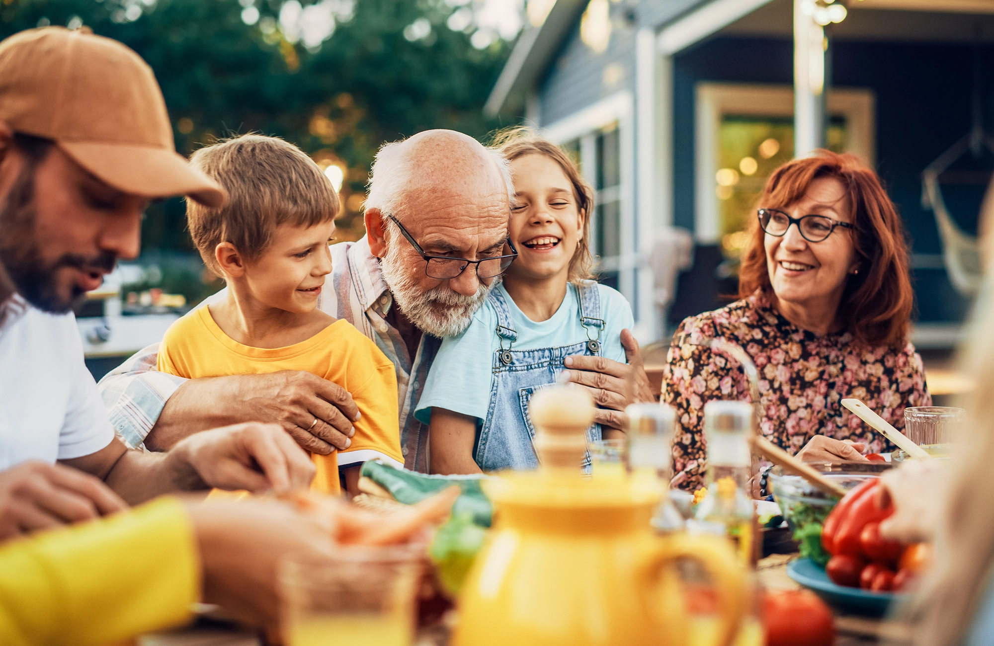 Mehrgenerationenfamilie sitzt zusammen an einem gedeckten Außentisch und genießt eine Mahlzeit in entspannter Atmosphäre.