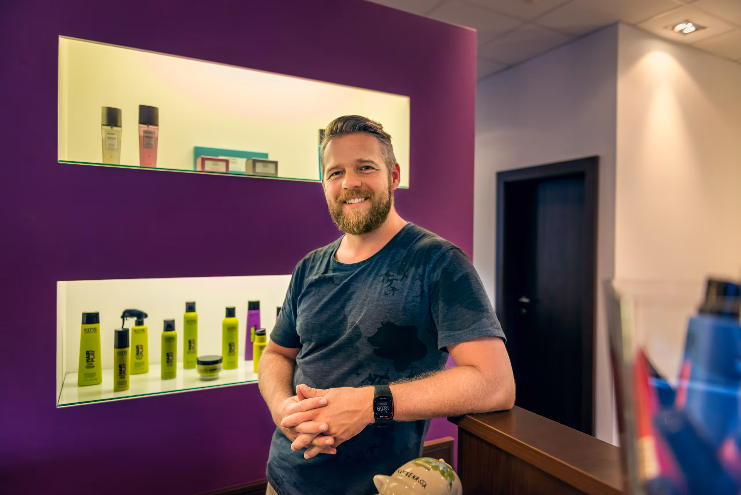 Portrait von Mike Zerzer der in die Kamera lächelt und am Empfangstresen des Friseursalons lehnt