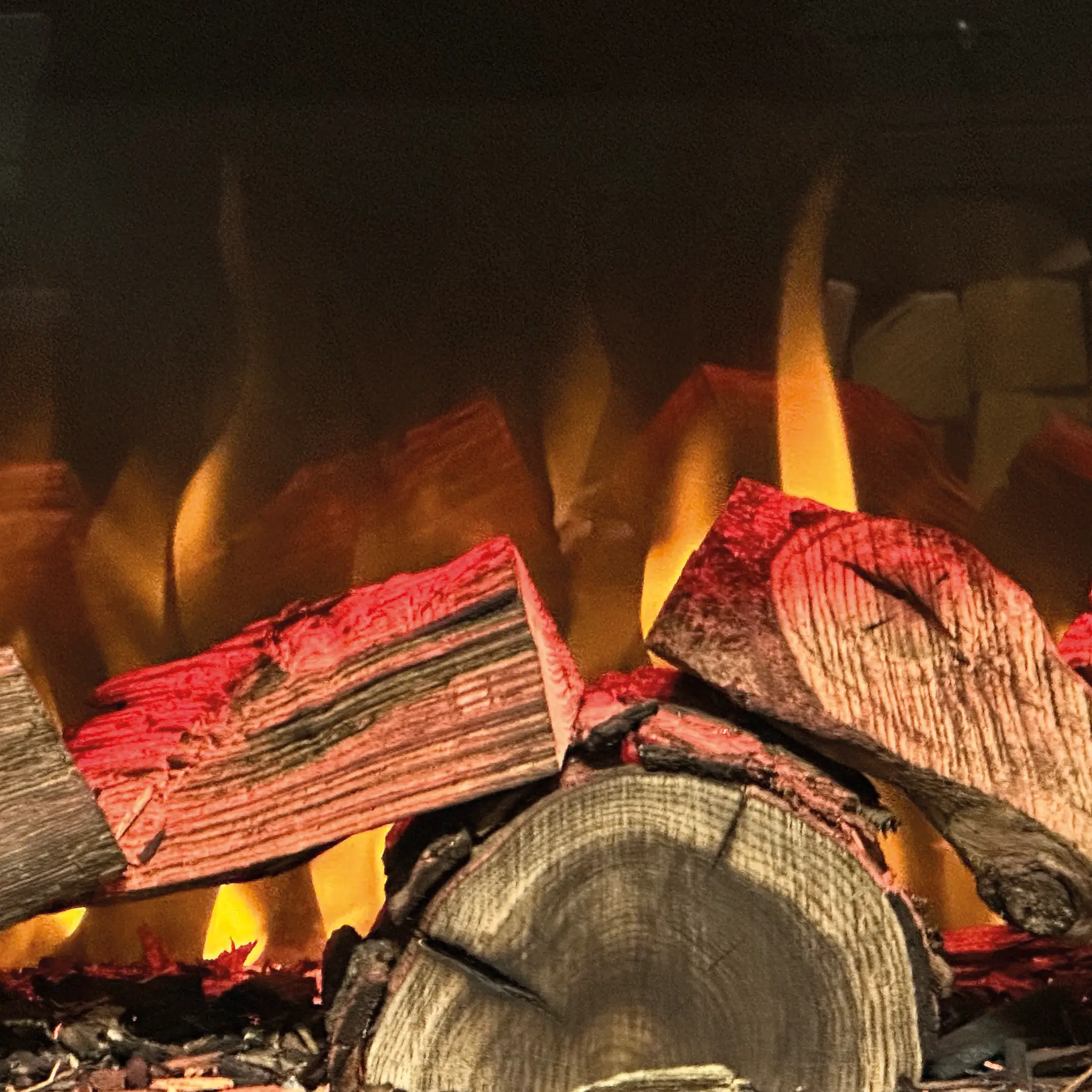 Close-up of burning firewood with bright yellow flames and glowing red embers on logs.
