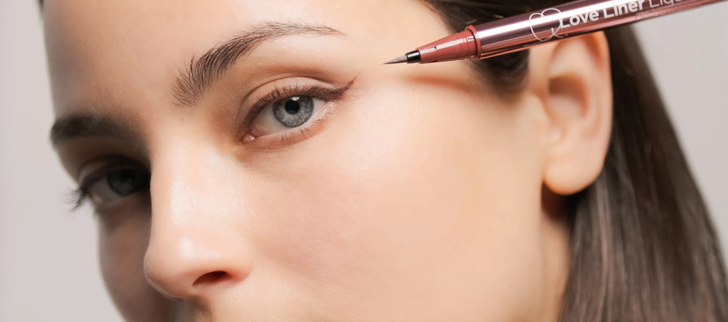 Close-up of a woman applying brown liquid Love Liner eyeliner to her upper eyelid wing.