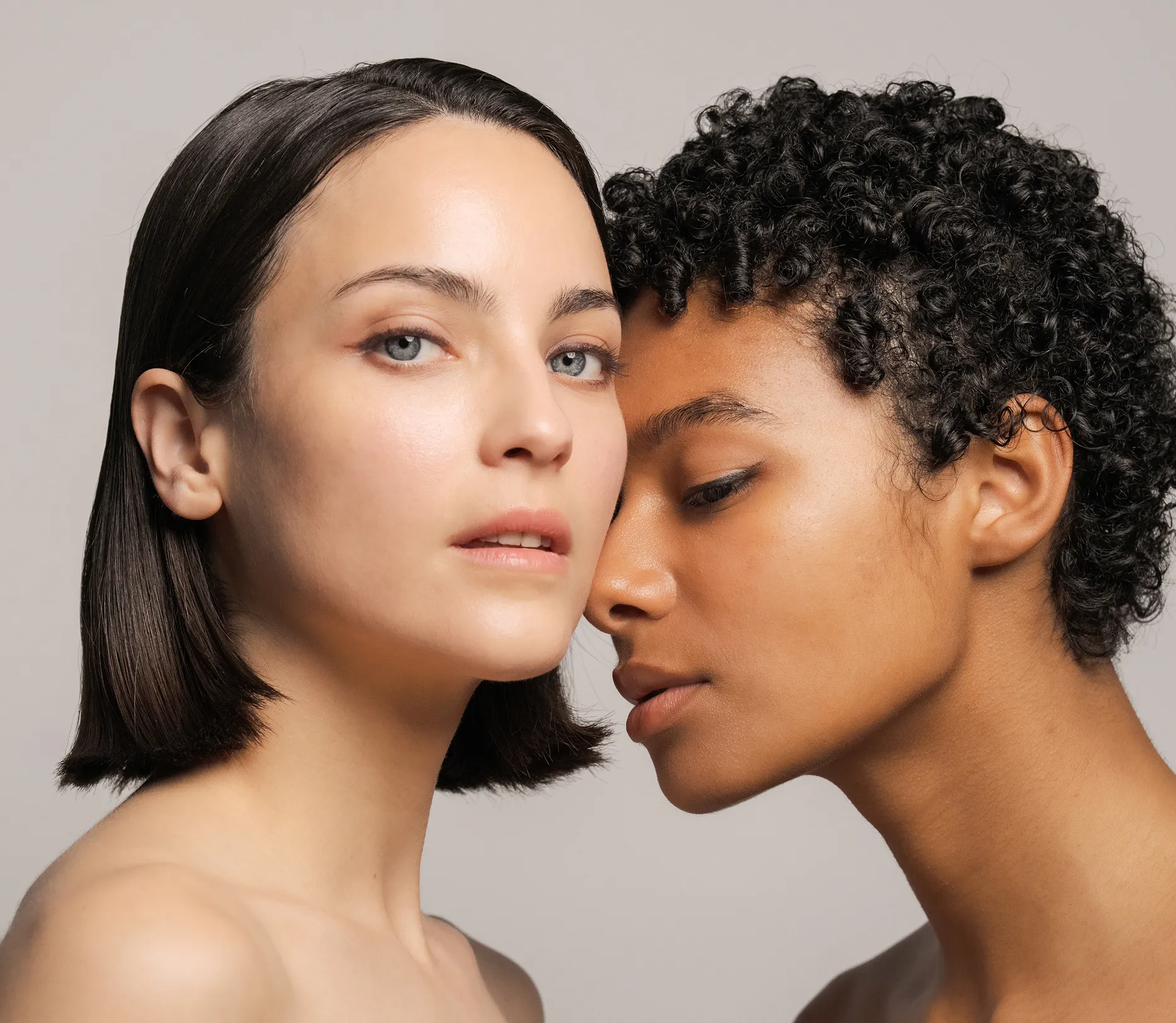 Close-up of two women with bare shoulders, one with short dark hair, the other with curly hair.