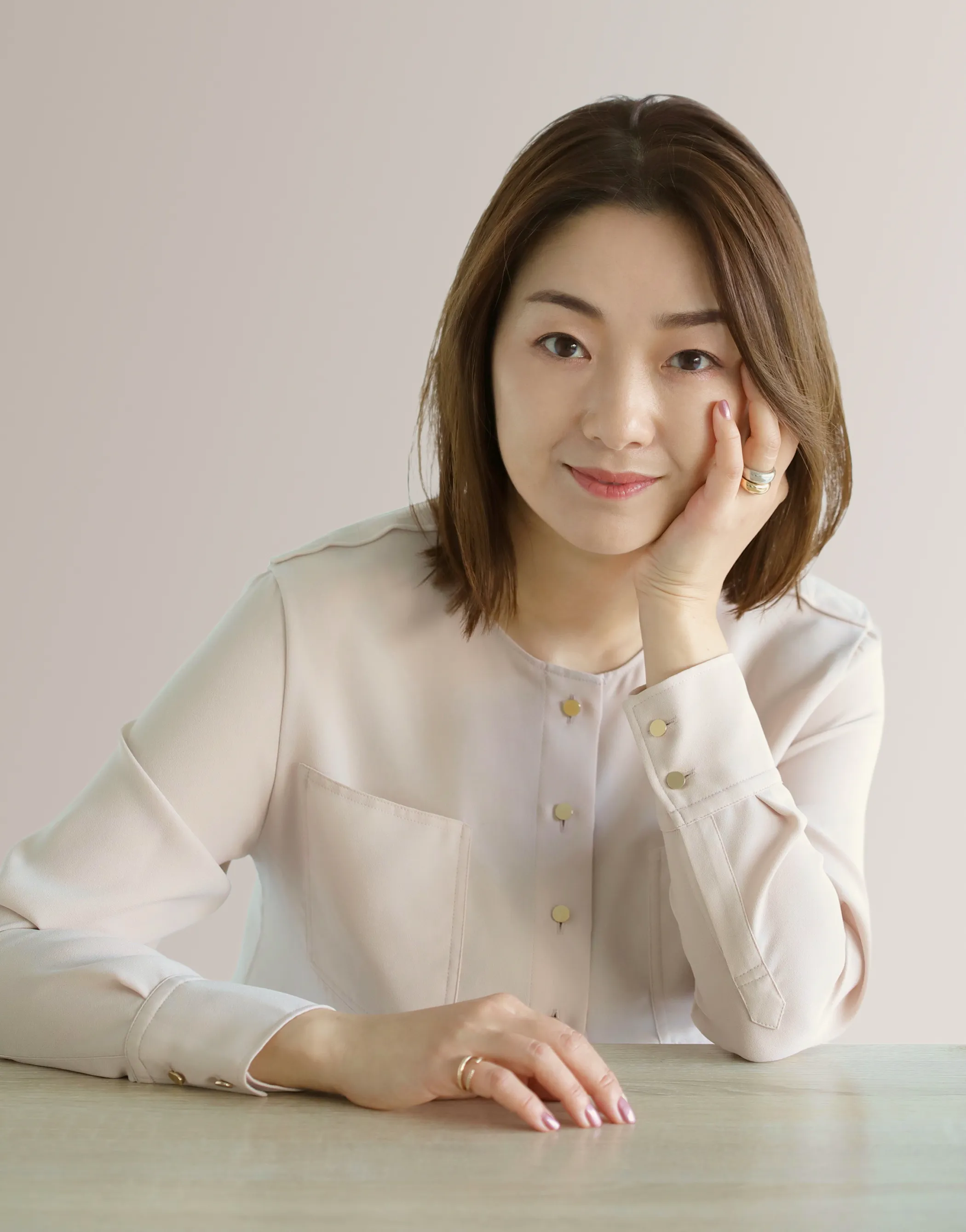 Smiling woman with brown hair resting her face on her hand at a wooden table, wearing a pale blouse. This women is the president of Love Liner : Tomomi Fujita.