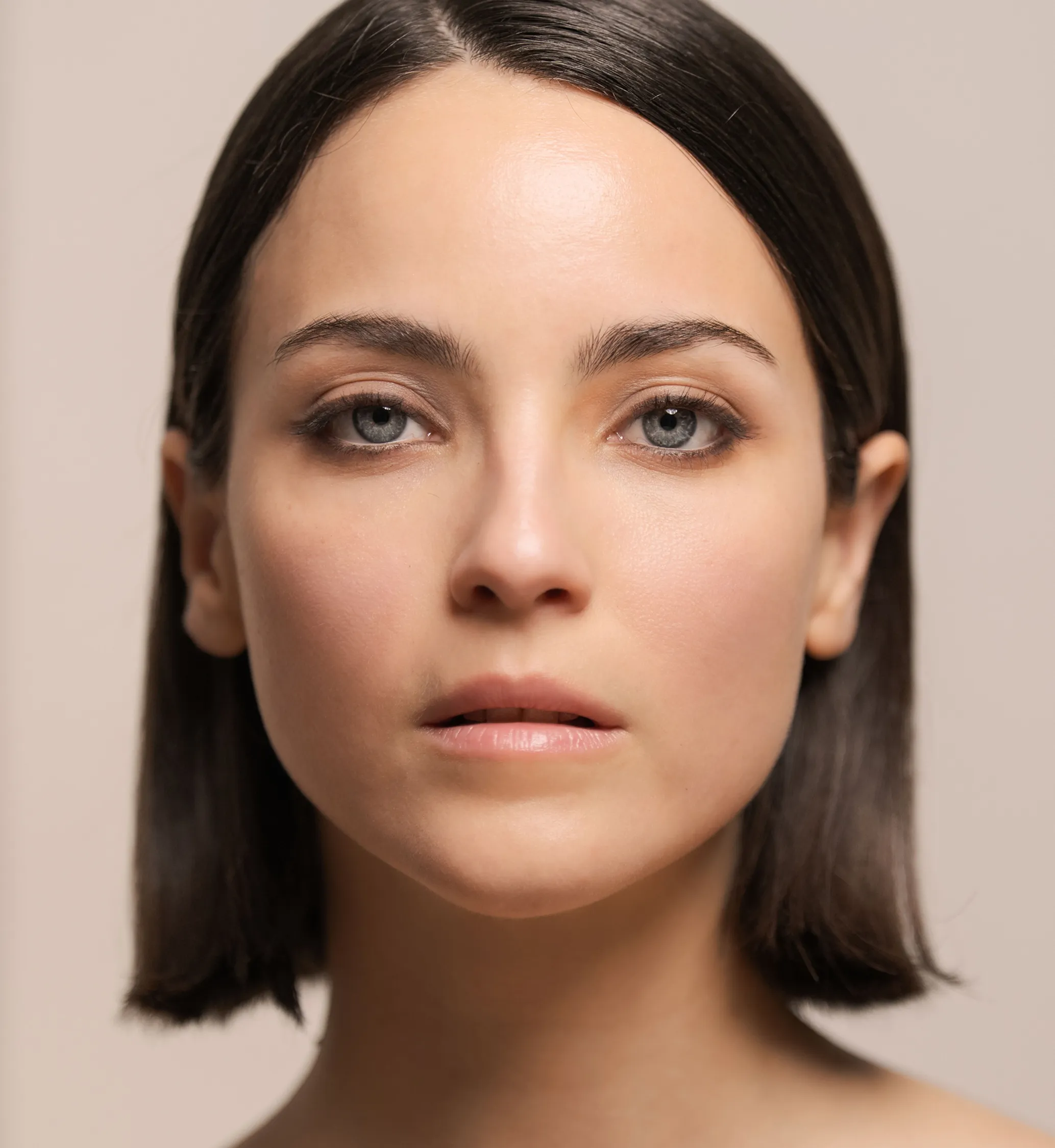 Close-up of woman with natural makeup and straight dark hair against a neutral background.