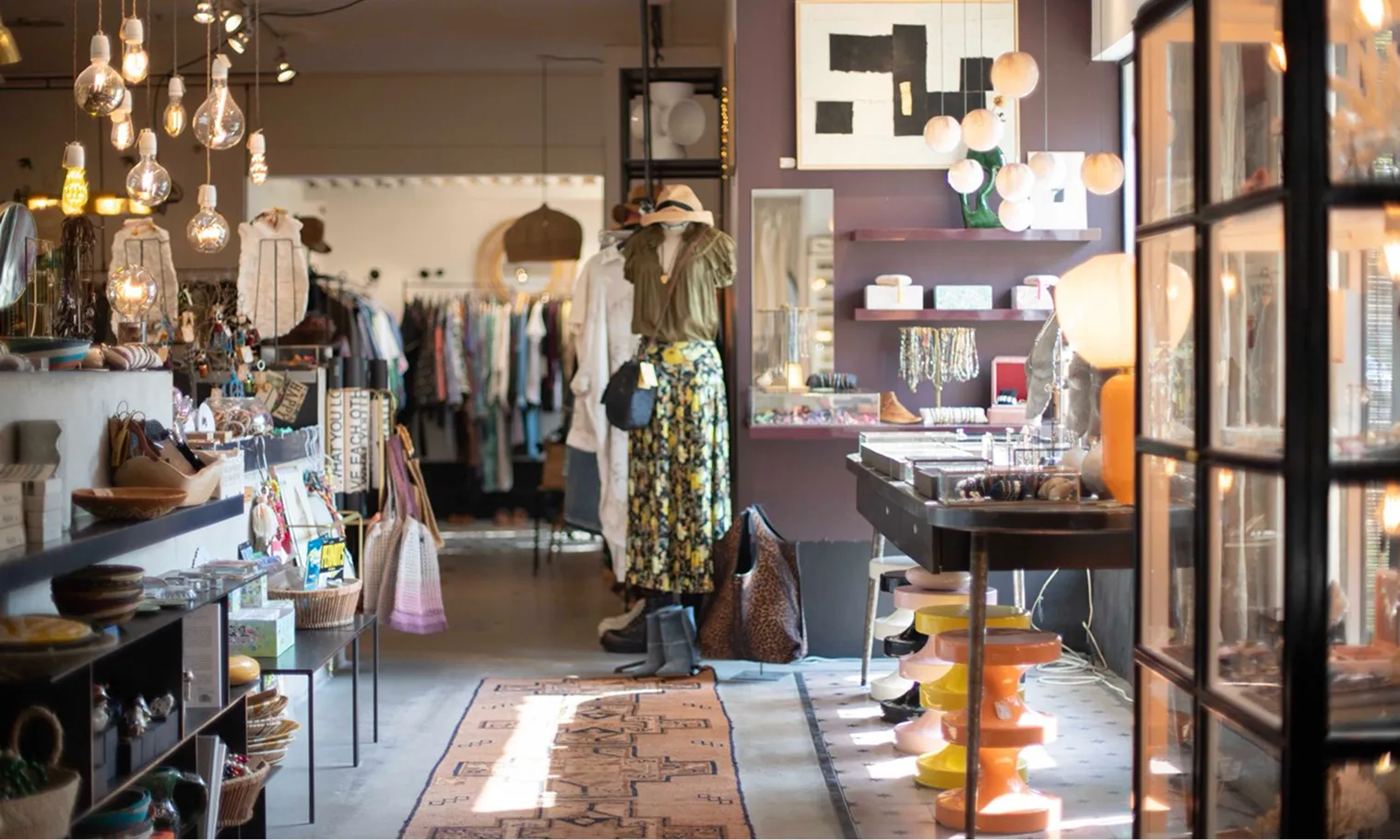 Interior view of a boutique with hanging lights, clothing racks, accessories, and decorative items.
