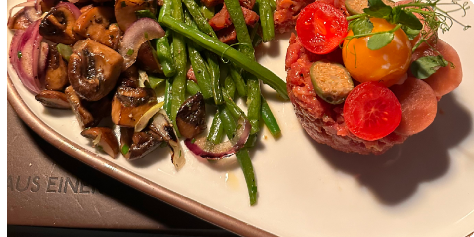 Plate with sautéed mushrooms and onions, green beans, and a round raw minced meat dish garnished with vegetables.