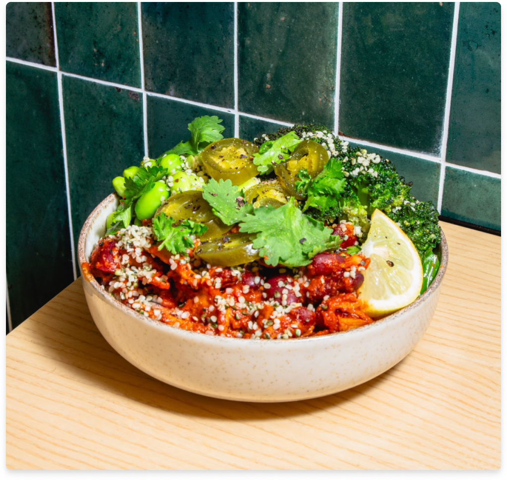 Bowl of broccoli, jalapenos, cilantro, lemon slice, red beans, and hemp seeds on a wooden table.