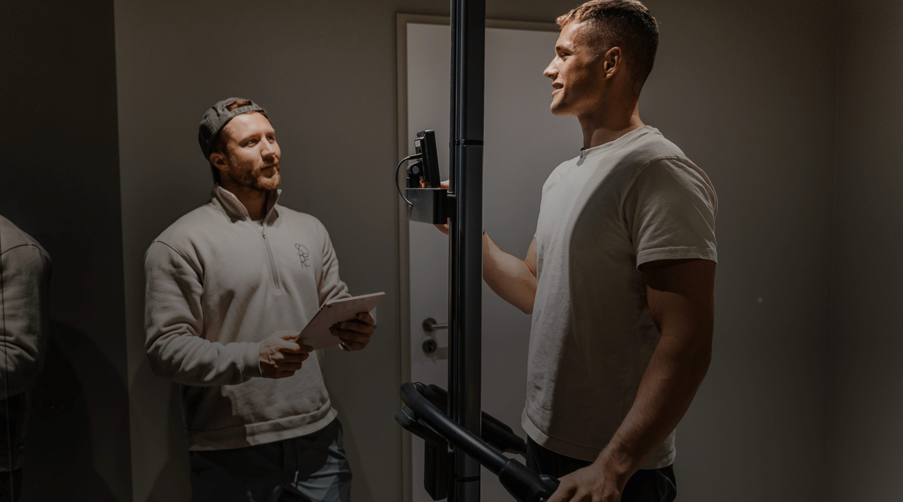 Trainer with clipboard observing a man using gym equipment for strength training.