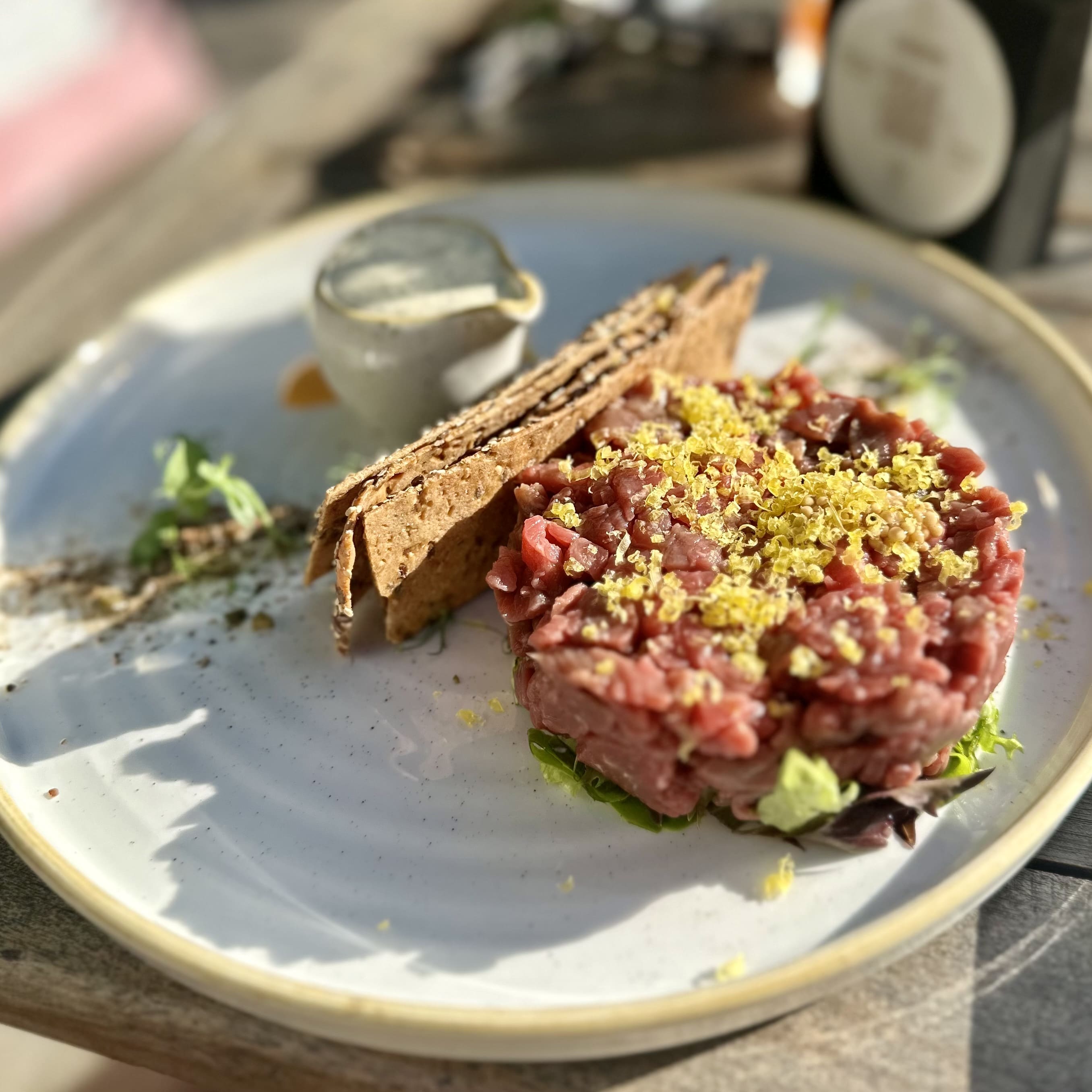Beef tartare topped with yellow garnish served with crispbread and sauce on a white plate.