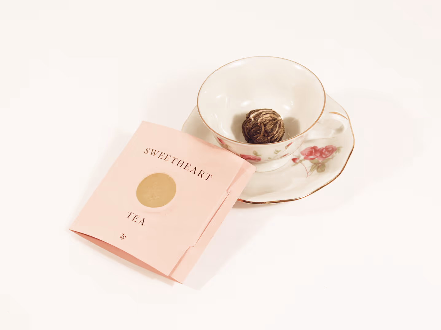 Sweetheart tea next to teacup with a floral design, blooming tea is inside.