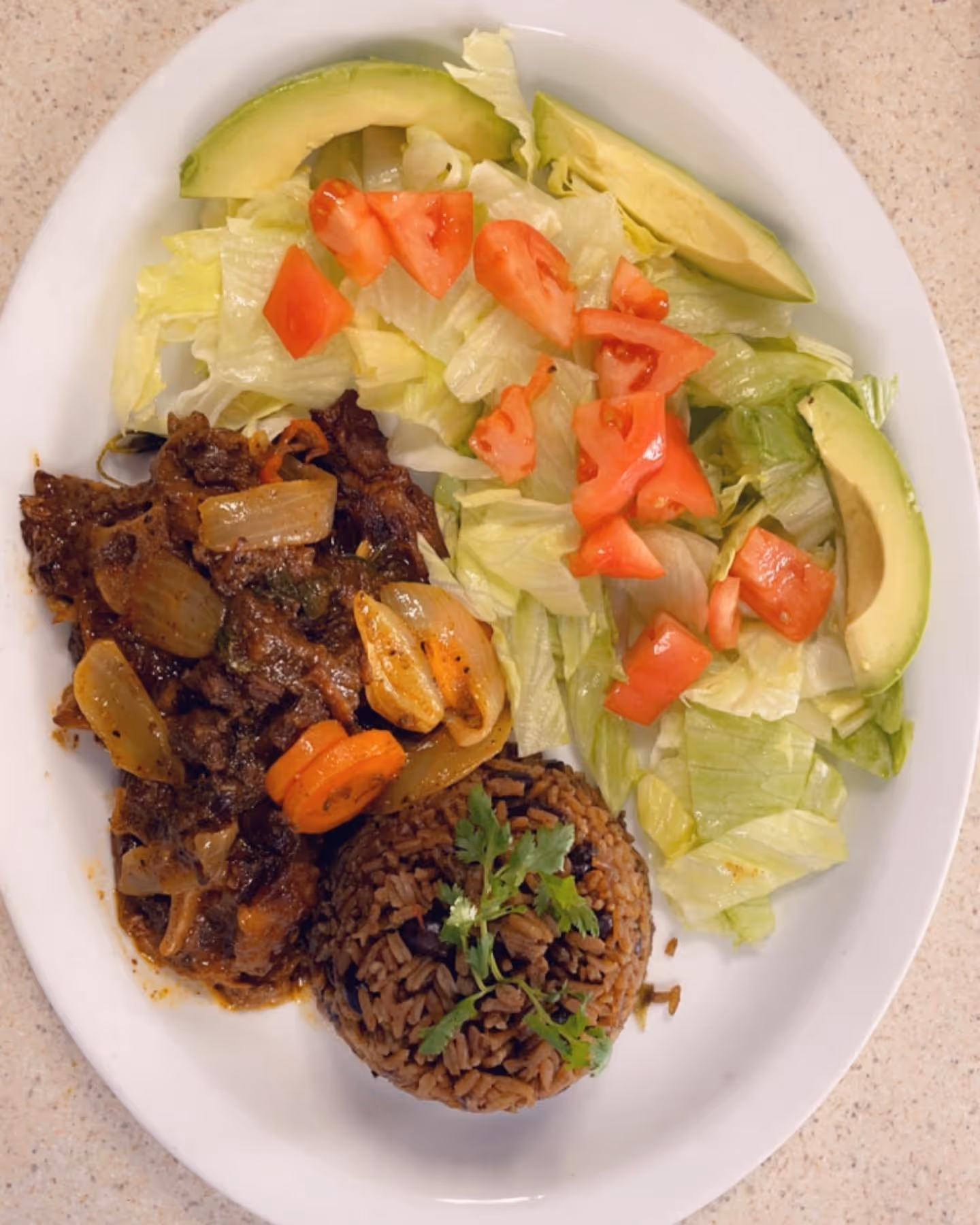 A plate of food with rice, meat, lettuce, tomatoes, and avocado.