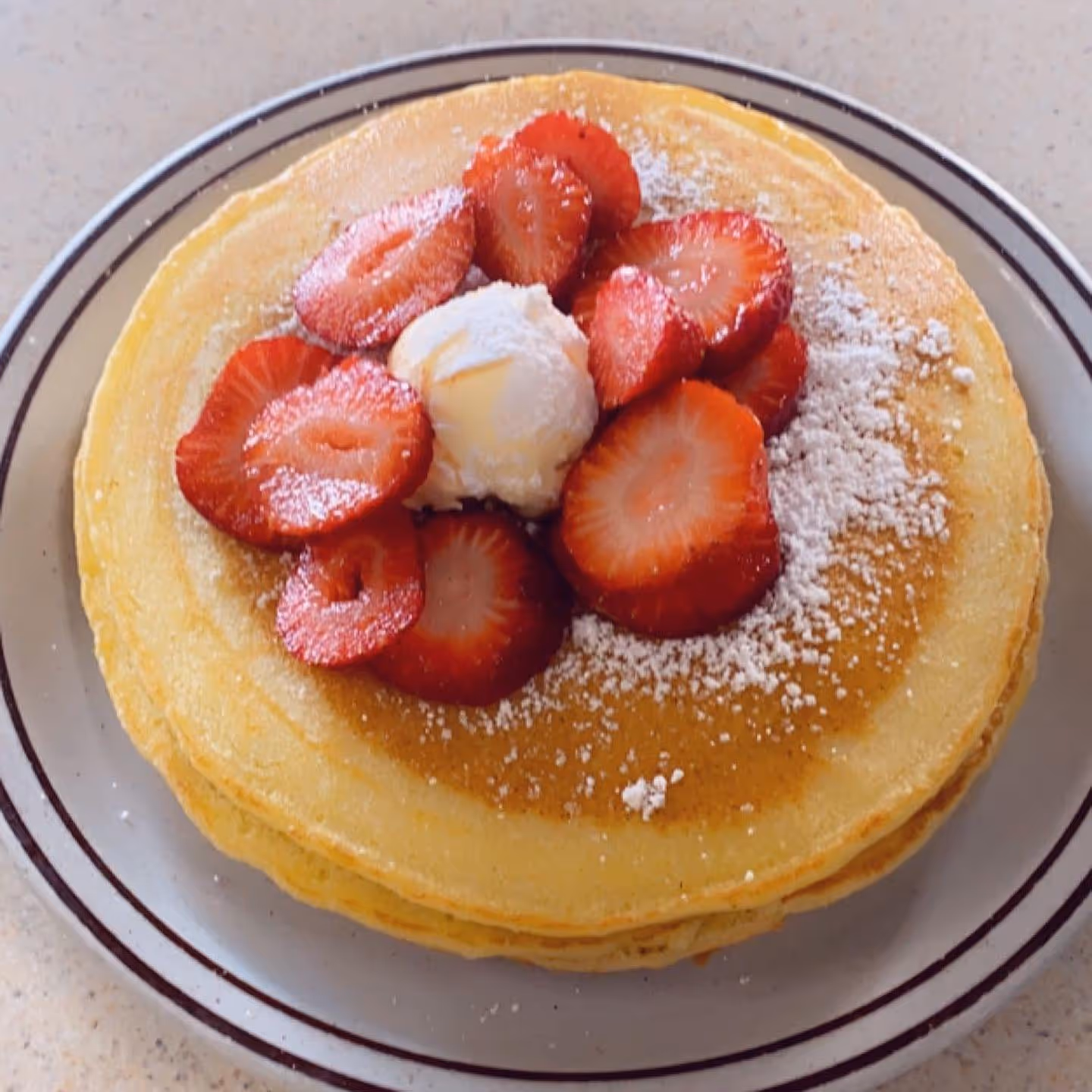 A stack of pancakes with strawberries and whipped cream on top.
