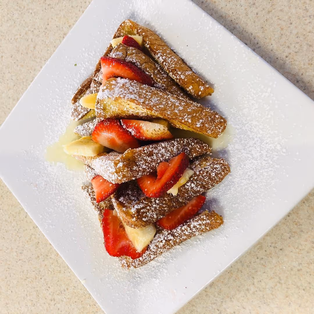 A plate of food with strawberries and powdered sugar.