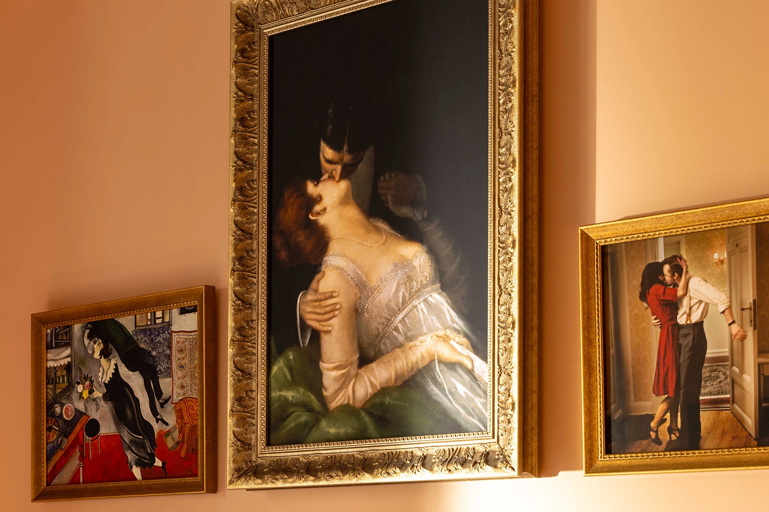 Chambre avec un lit double fait avec des draps blancs et des oreillers rouges, une couverture rouge, une table de chevet avec une lampe, et des tableaux accroché au mur.