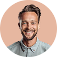Smiling man with light brown hair and beard wearing a buttoned shirt against a peach background.
