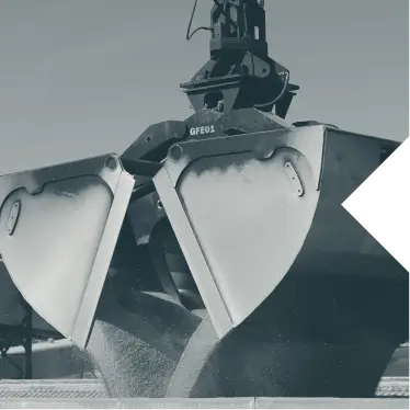 Industrial clamshell bucket unloading bulk material on site under clear sky.