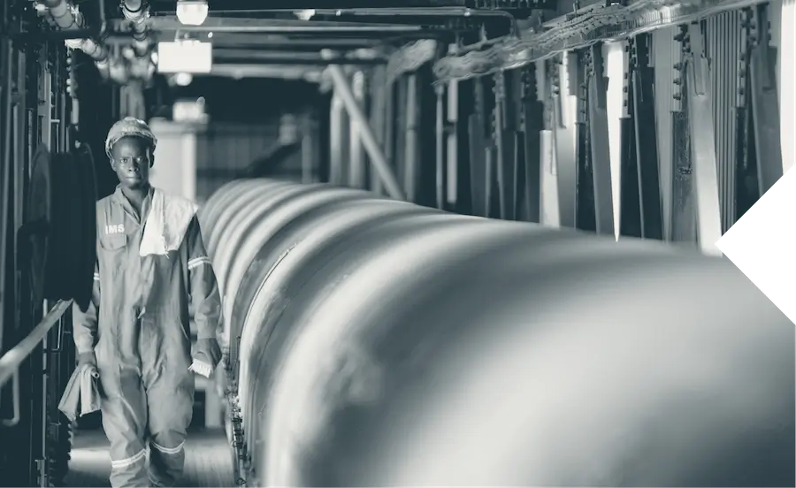 Engineer in safety gear walking beside large industrial pipes in a factory facility.