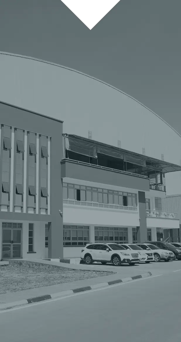 Modern commercial building with large windows and a curved roof, with five parked cars in front on a sunny day.
