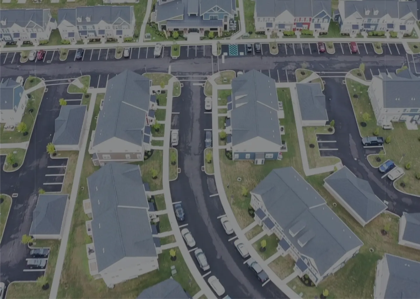 Aerial view of a residential neighborhood with townhouses, roads, sidewalks, and parked cars.