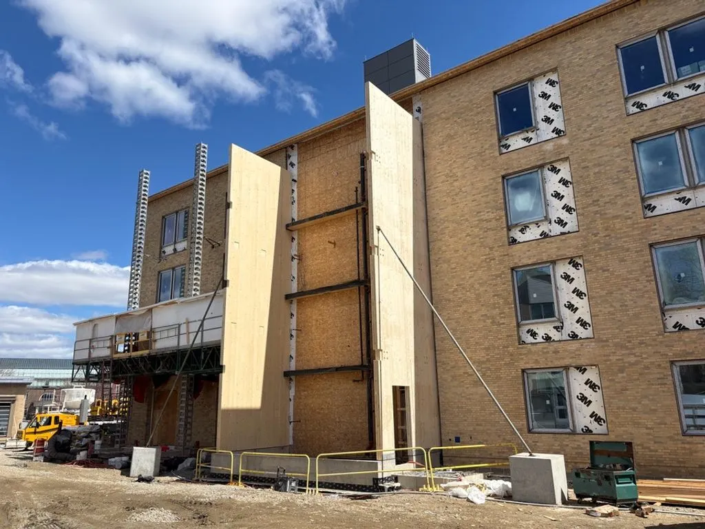 A large building under construction, with wooden panels and scaffolding visible on the exterior.