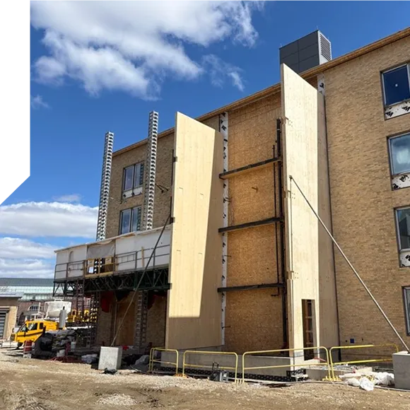 Construction site of a building with a wooden facade being installed, surrounded by scaffolding and barriers.