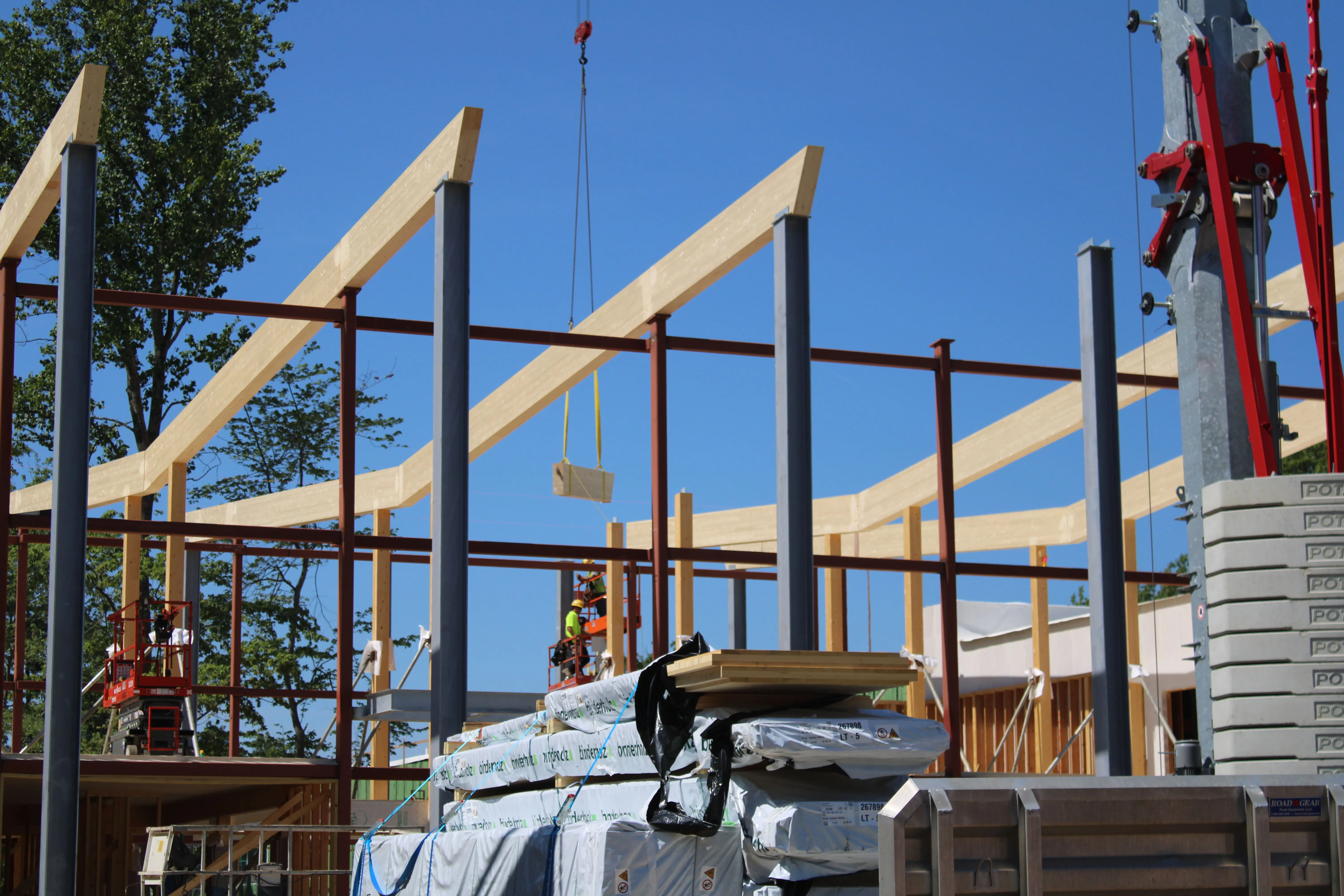 Construction site with steel and wooden beams being lifted under a clear blue sky.
