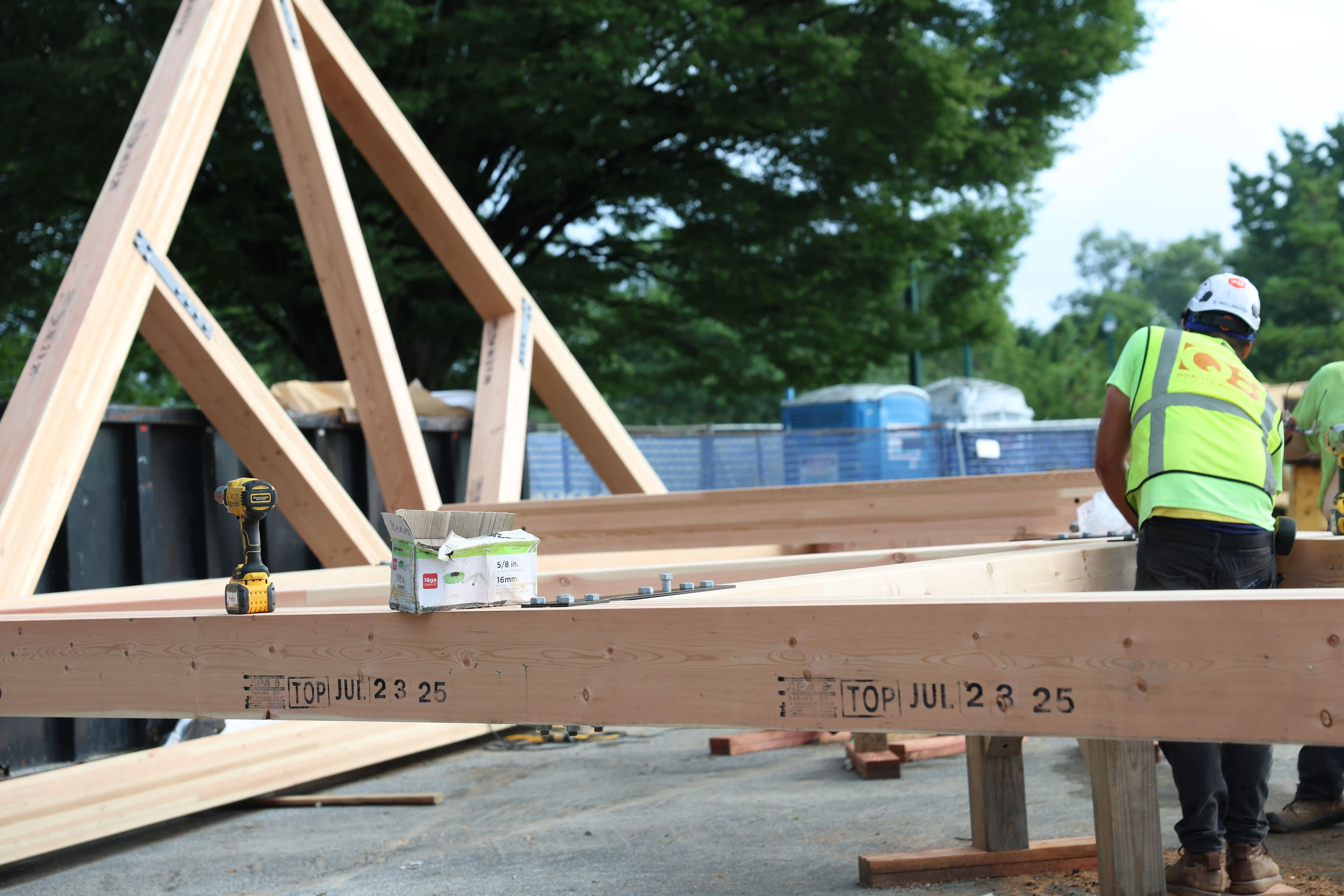 Construction workers assembling wooden beams and trusses outdoors at a building site.