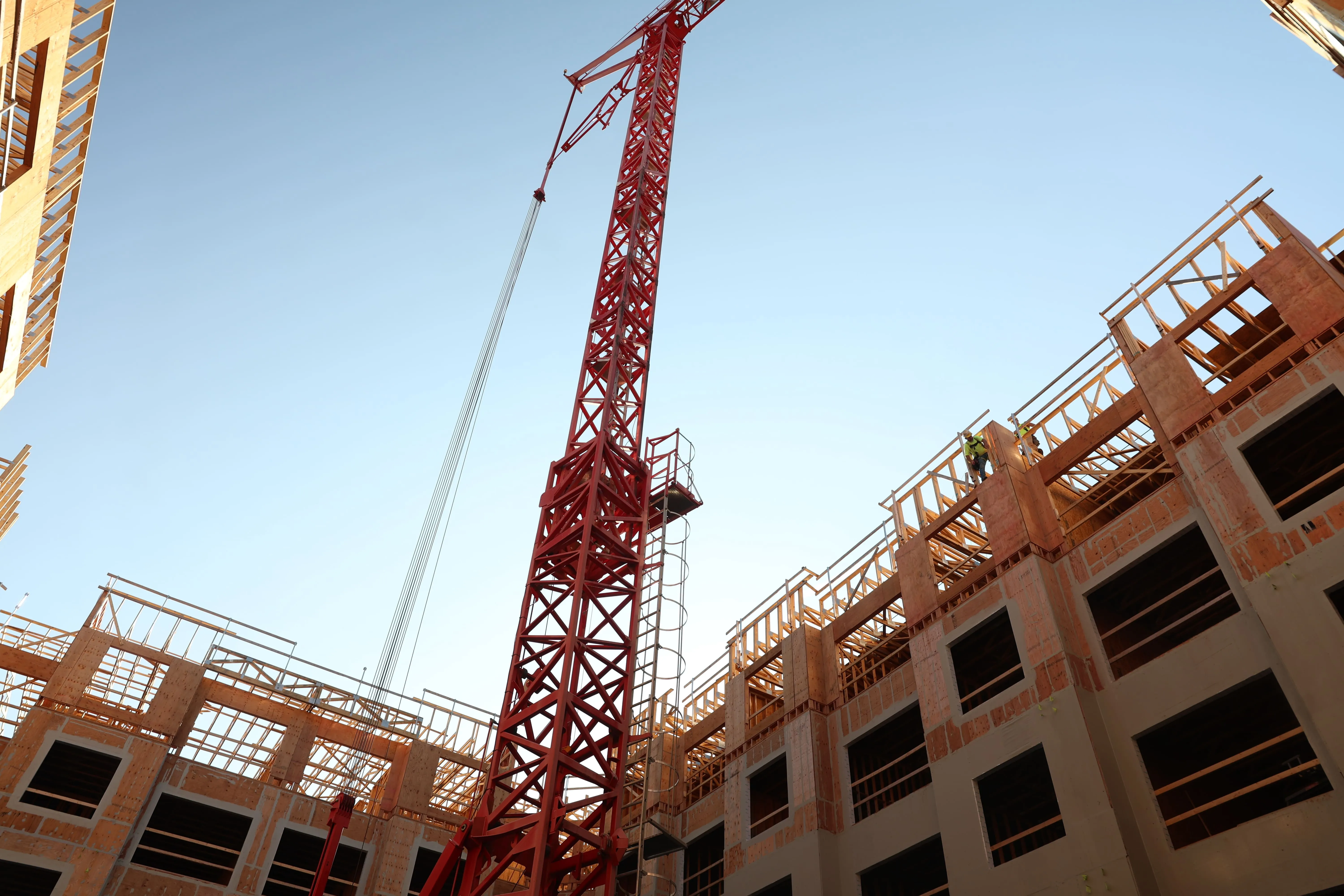 Red construction crane tower inside a building under construction with wooden framework and workers.