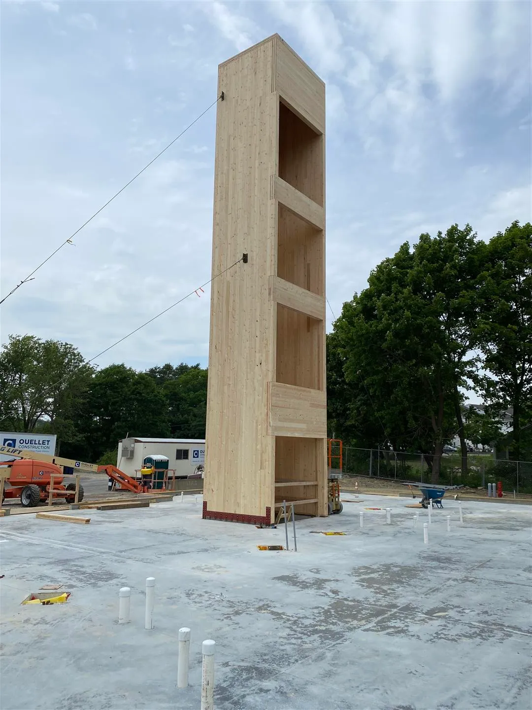 A tall wooden structure under construction stands on a concrete foundation at a building site.